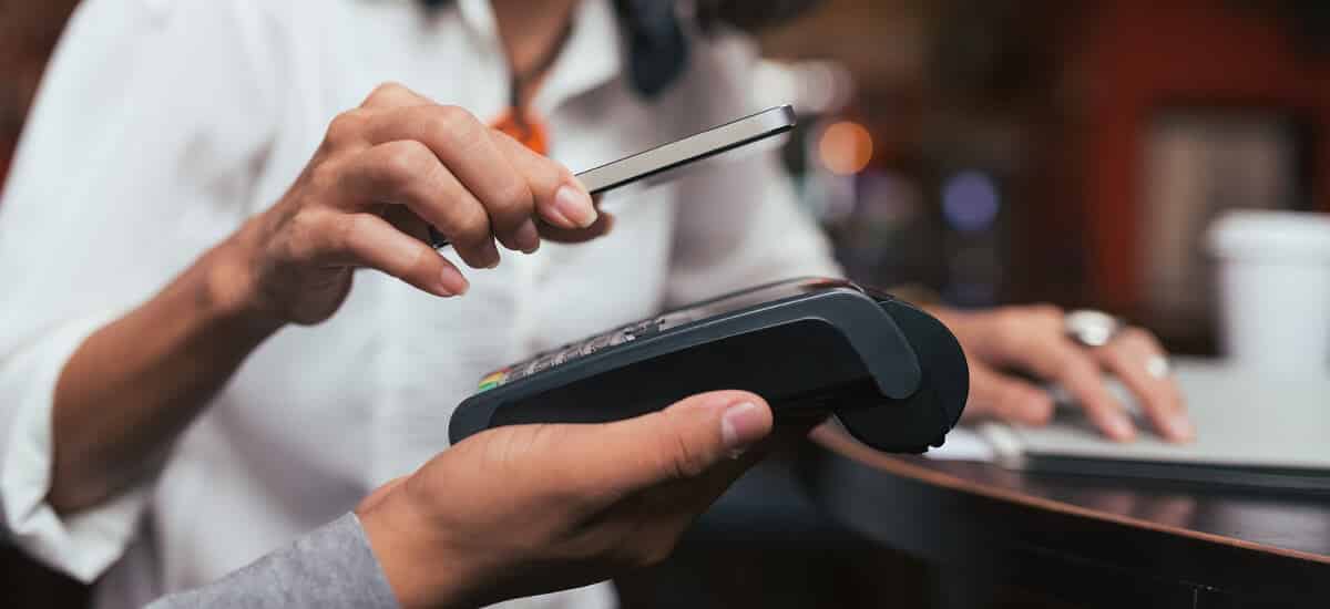 Mão segurando celular enquat outra segura máquina de cartão para pagamento via NFC