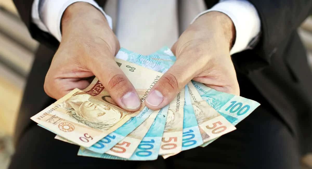 Mão mostrando diversas cédulas de dinheiro