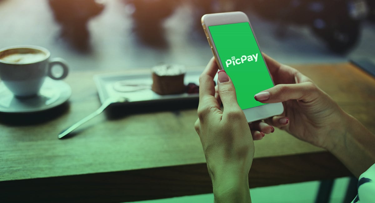 Mãos segurando celular com app PicPay sobre mesa de café