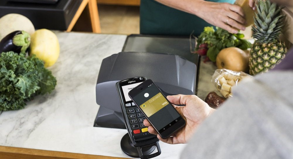 Mão fazendo pagamento com Android Pay em frutaria