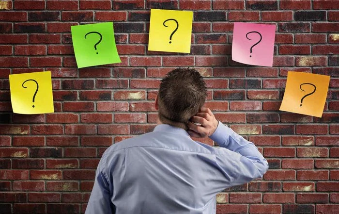 Homem olhando para cartões coloridos com interrogações em uma parede