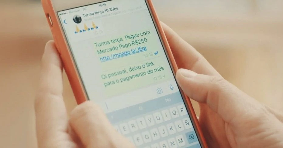 Mão segurando um smartphone com a tela mostrando um link de pagamento do Mercado Pago enviado por rede social