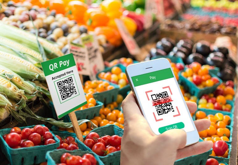 Pessoa escaneando com celular o QR Code de tomates em uma bancada de legumes