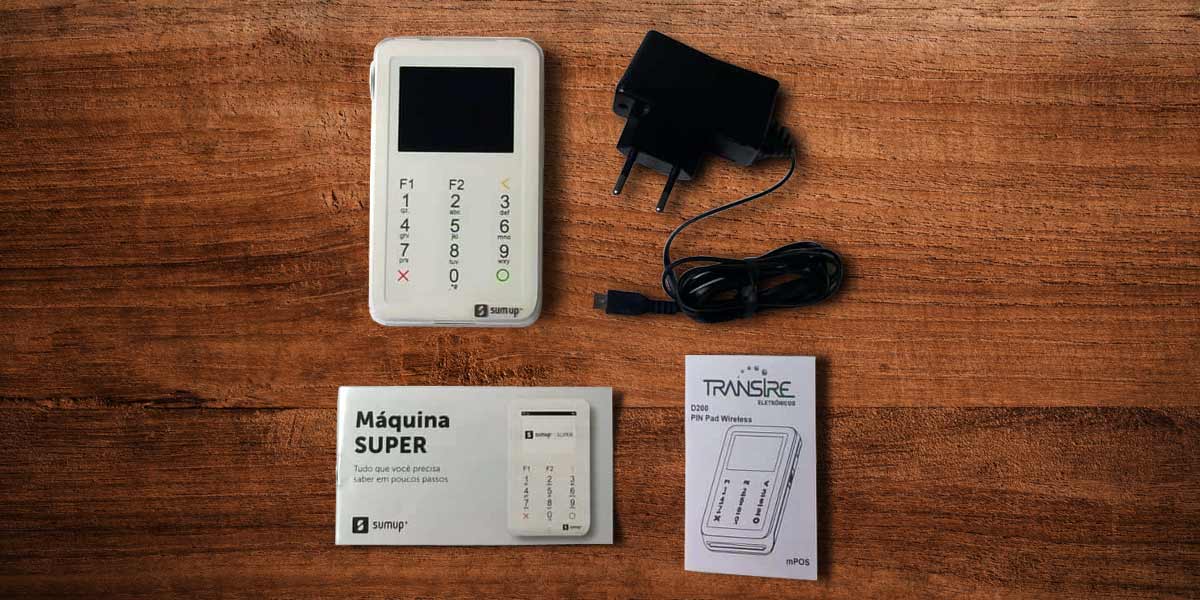 Itens encontrados na caixa da SumUp Super: máquina, manuais e cabo USB em cima de uma mesa