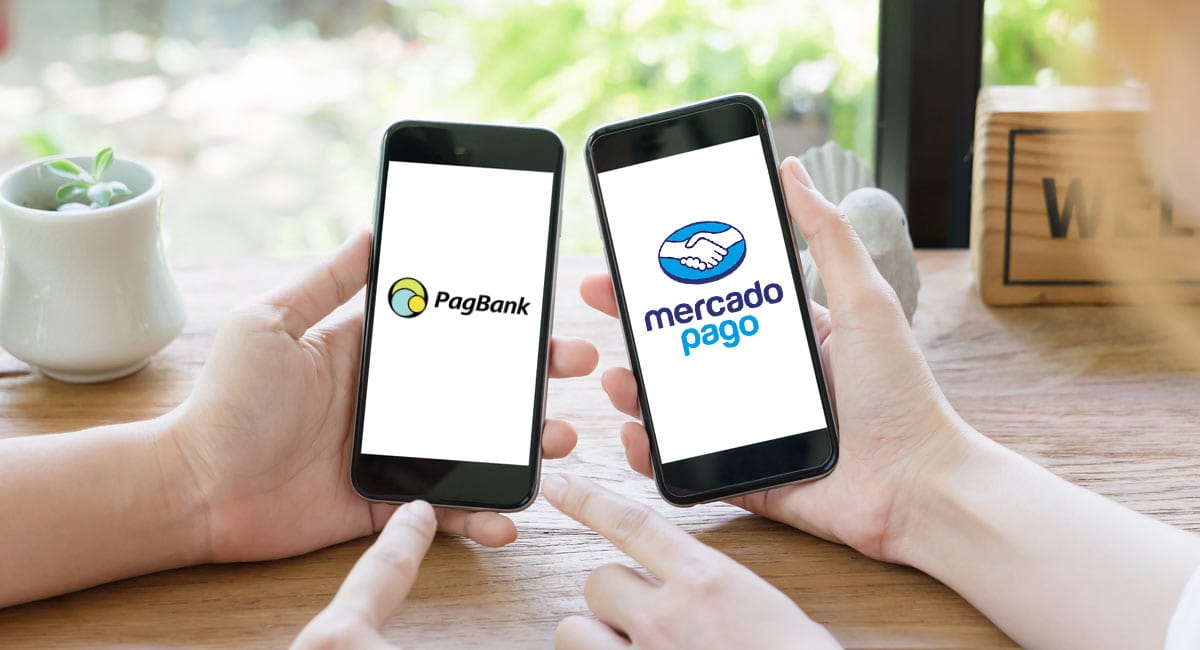 Mãos segurando celulares e mostrando na tela logos do PagBank e Mercado Pago