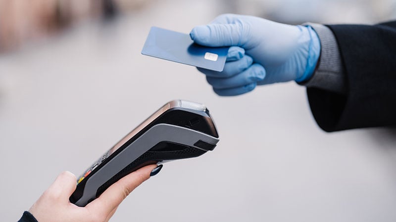 Mão com luva de borracha segurando cartão em frente à maquina de cartão